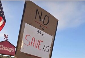 Protest sign reads "NO to the SAVE Act."